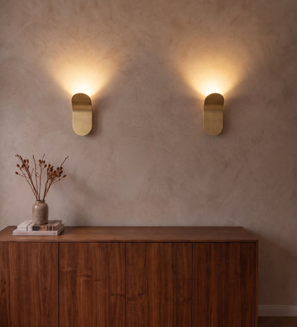 Two Vela wall lights in brushed gold washing warm light up the wall above a sideboard
