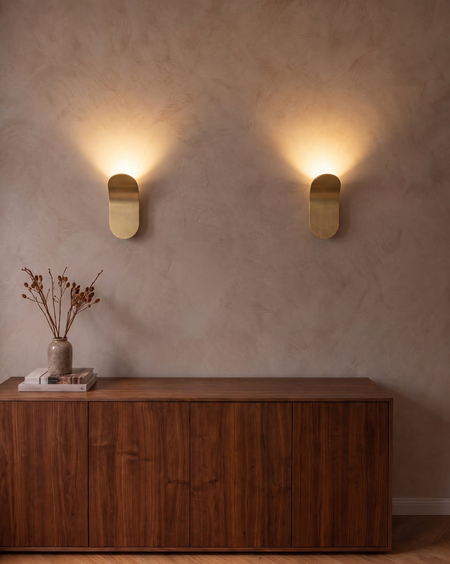 Two Vela wall lights in brushed gold washing warm light up the wall above a sideboard