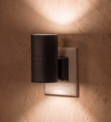 Nido plug-in wall light in black, plugged straight into a UK 3-pin socket, warm light up and down the wall