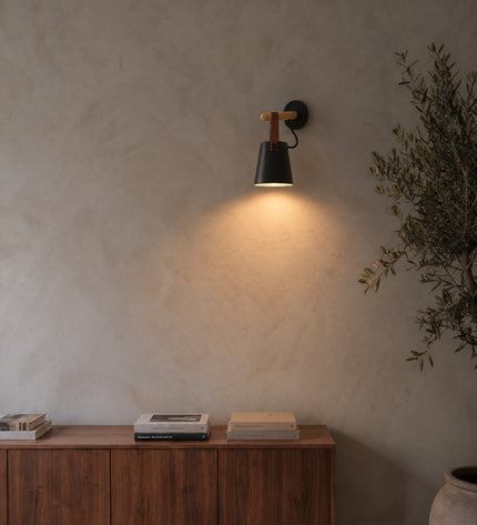 Monaco wall light in black with wooden rod and leather strap on a lime plaster wall
