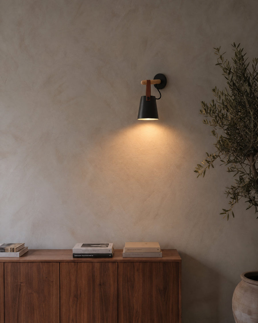 Monaco wall light in black with wooden rod and leather strap on a lime plaster wall