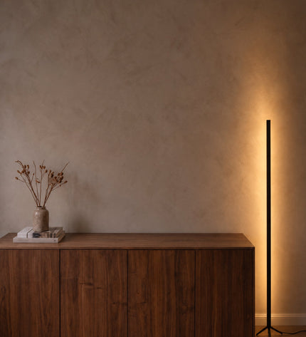 Sento floor lamp in black next to a sideboard, casting indirect light on a lime plaster wall