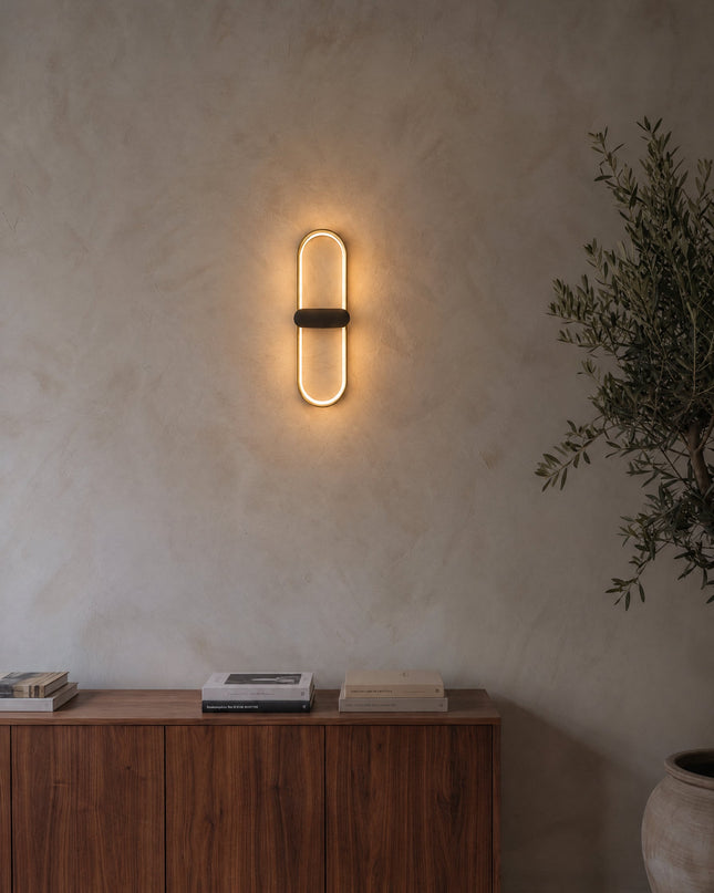 Lunaris Wandleuchte in Gold und Schwarz an einer Kalkputzwand