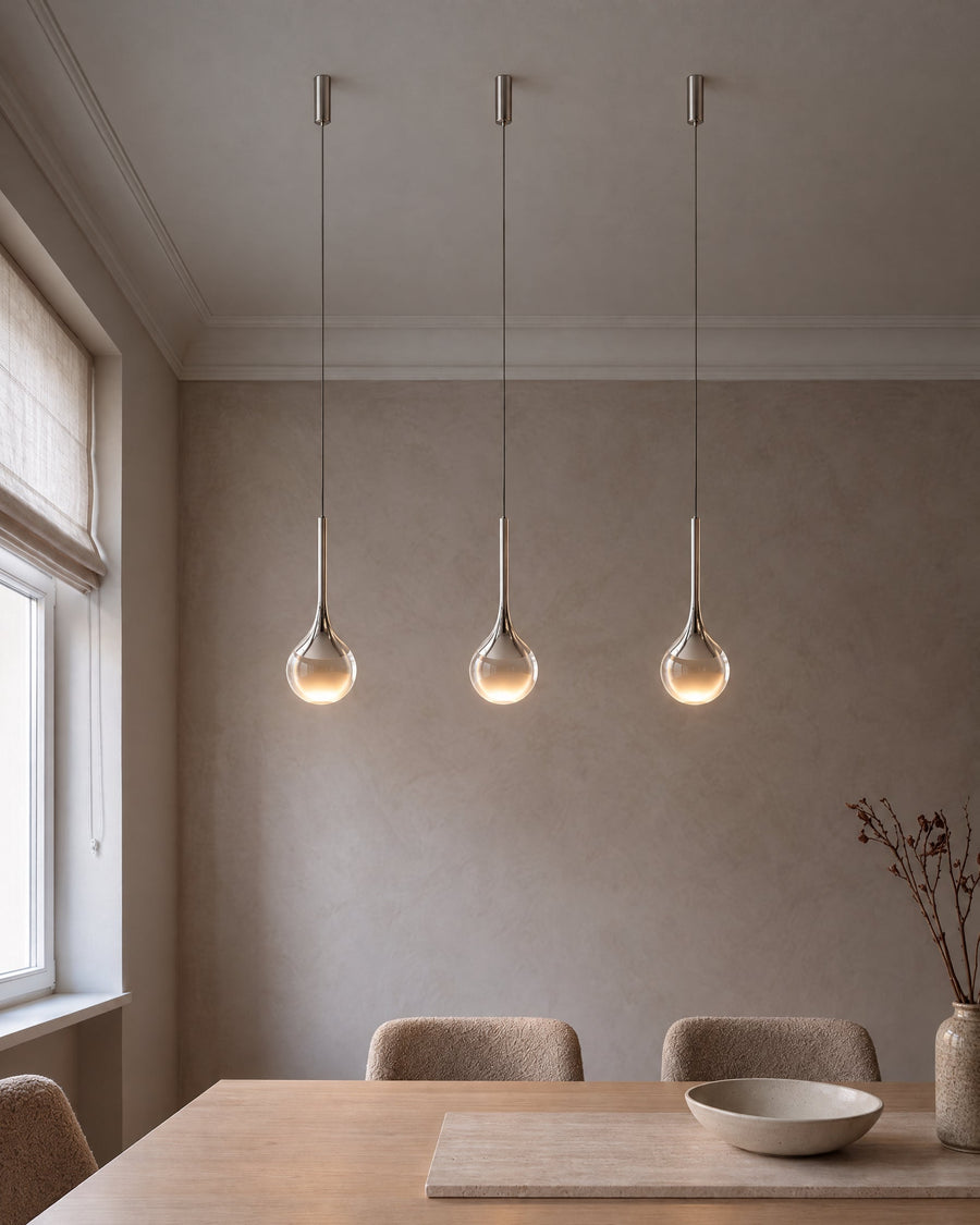 Three Gota pendant lights in chrome above a dining table