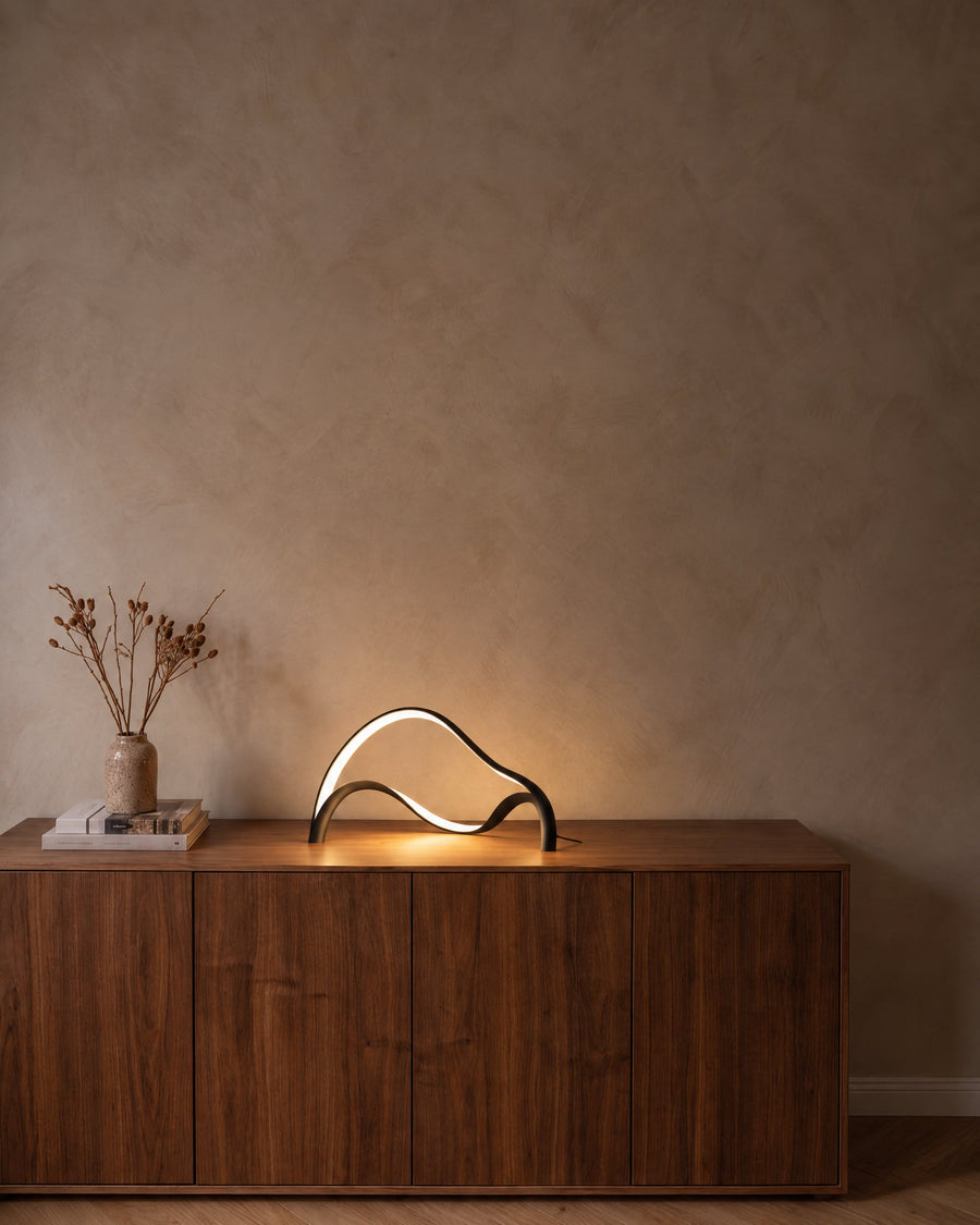 Volta sculptural LED table lamp in matt black on a walnut sideboard