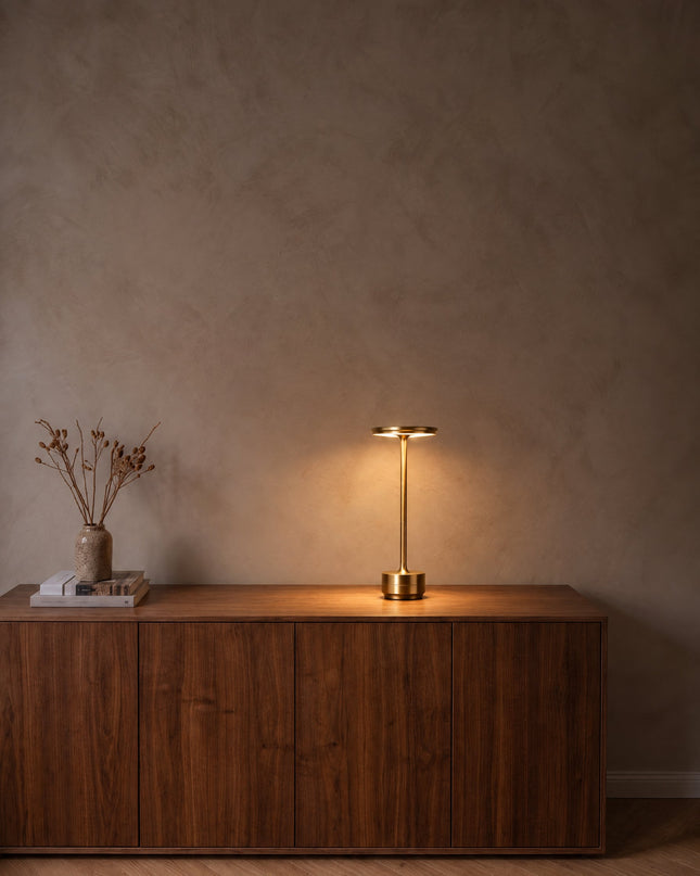 Lido cordless table lamp in gold, switched on, on a walnut sideboard