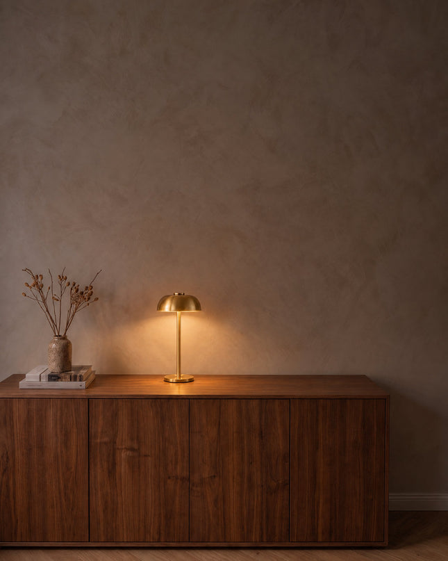 Bolla cordless dome table lamp in gold, switched on, on a walnut sideboard