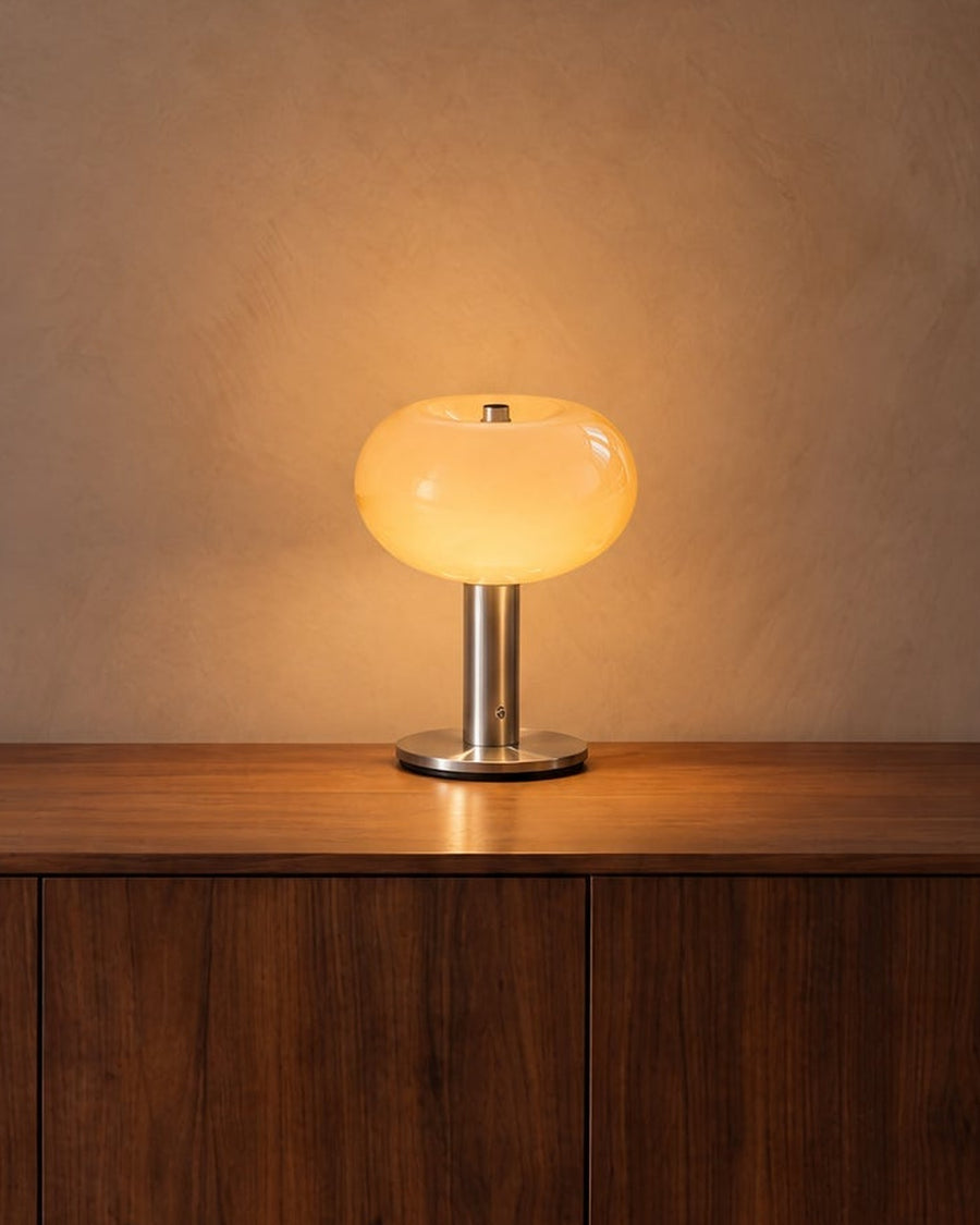 Mela table lamp with amber glass shade and silver base, switched on, on a walnut sideboard
